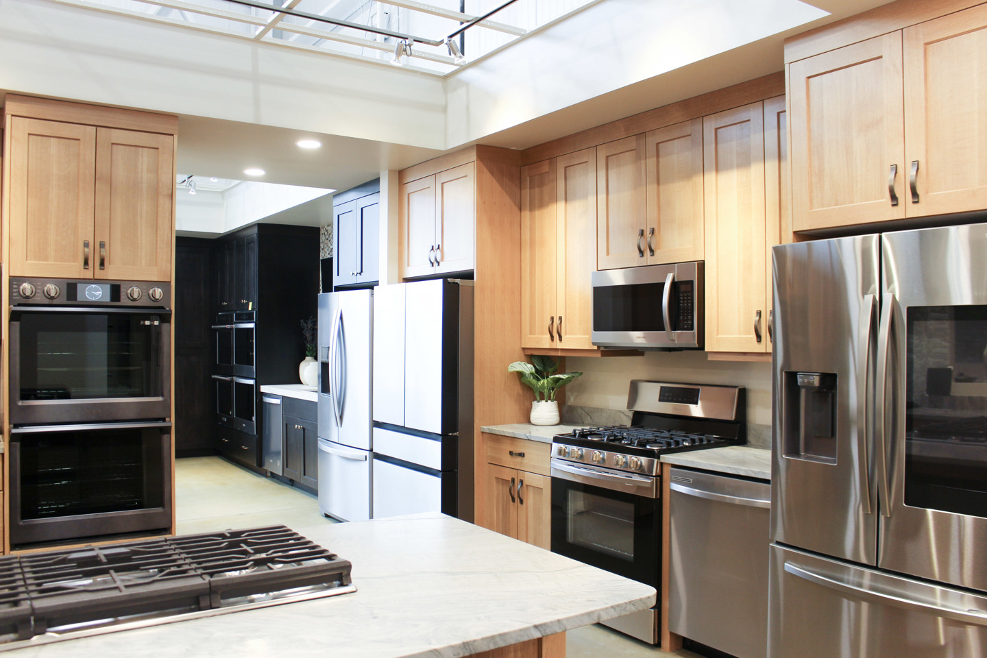 Appliance showroom with stainless-steel refrigerators, ovens and a range set among wood cabinets.