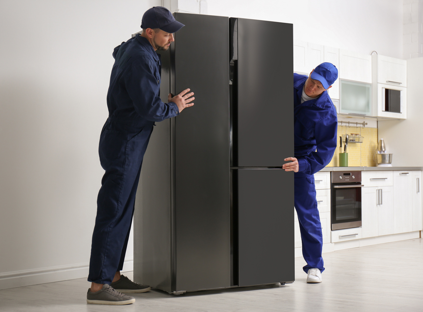 Two delivery workers positioning a refrigerator in a kitchen.