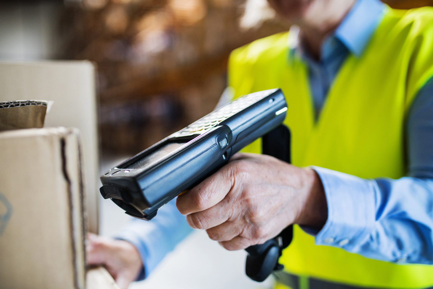 Warehouse worker holding a handheld barcode scanner beside cardboard boxes.